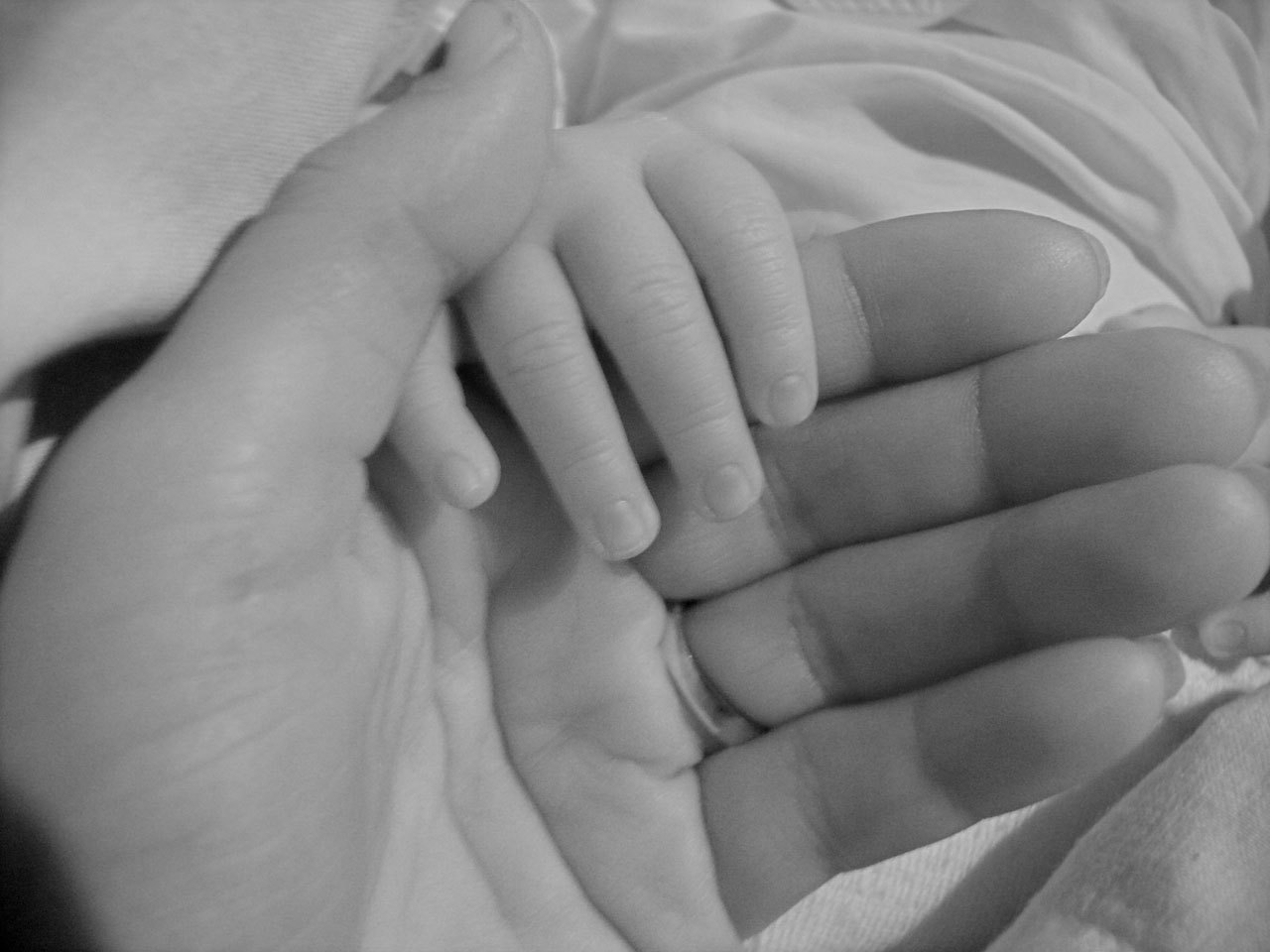 Black and white image of a baby's hand wrapped around the mother's index finger, middle finger, and palm.