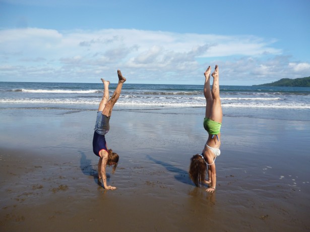 Two girls doing handstands on a beach.