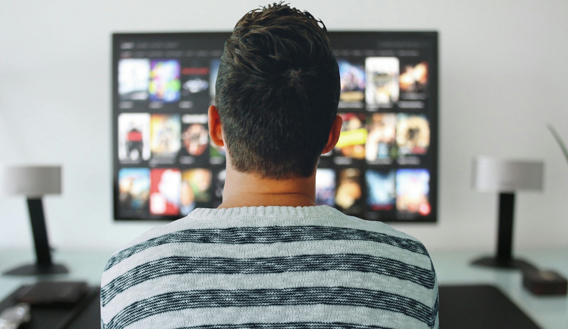 Back of man's head as he looks at a TV screen with many watching options to choose from